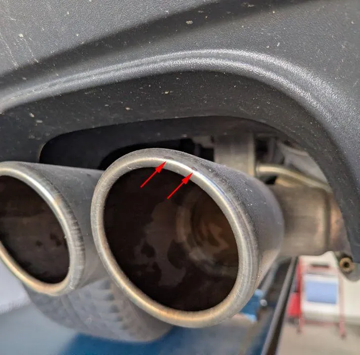 Dual tailpipe seen from below, red arrows marking impact marks on the tailpipe trim