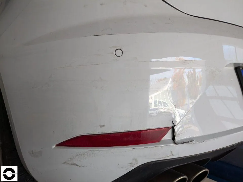 White rear left bumper torn and scraped, with a scraped parking sensor above it
