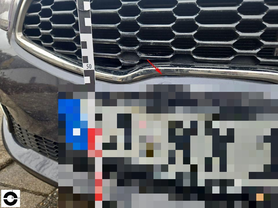 Frontansicht Kühlergrill mit Messlineal, roter Pfeil markiert Kratzer an Chromleiste