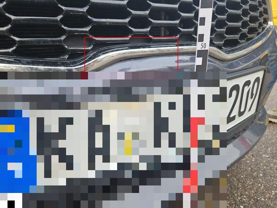 Frontpartie mit Kühlergrill, Messlineal zeigt Schadensbereich, Kennzeichen pixeliert