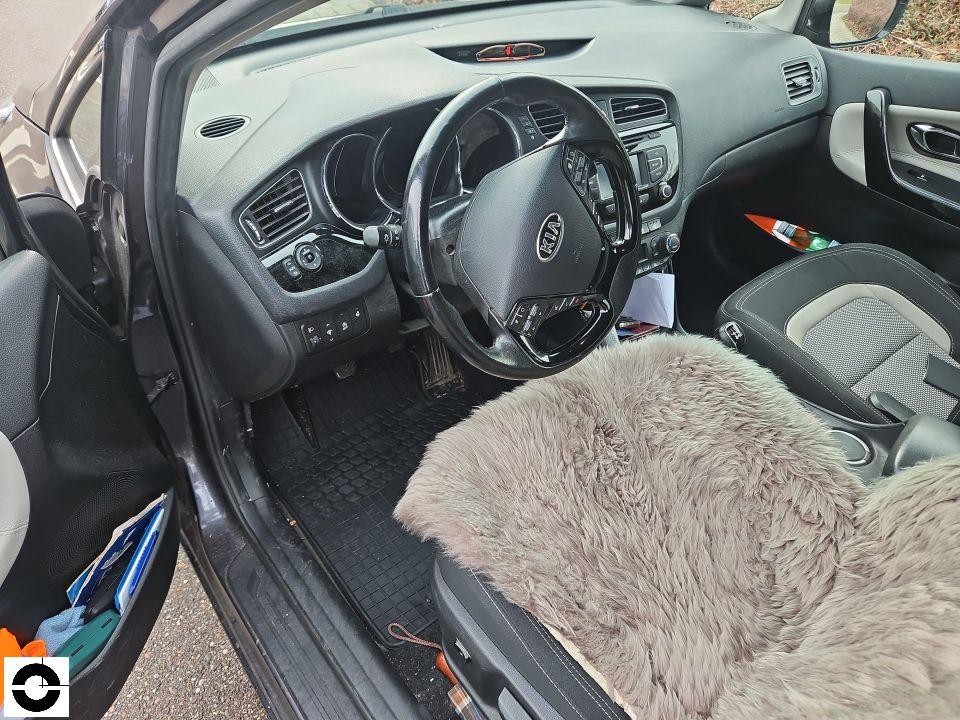 Innenraum Fahrerseite, KIA-Lenkrad, Fellfell-Sitzauflage, schwarzes Armaturenbrett, geöffnete Fahrertür