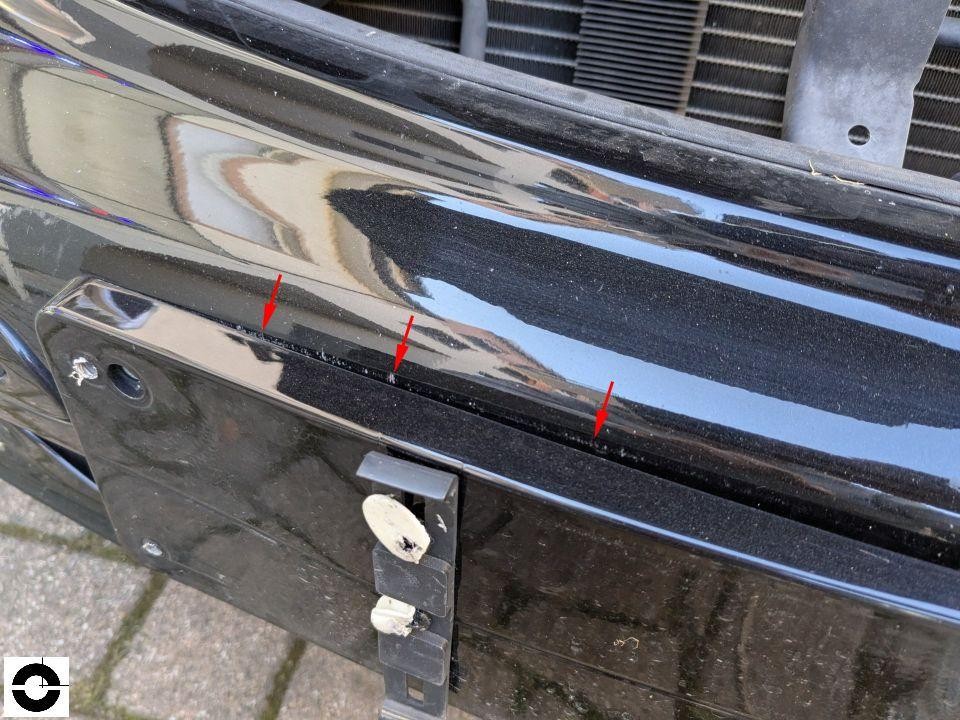 Detailaufnahme Frontstoßstange schwarz mit roten Markierungspfeilen auf Kratzer und Lackschäden