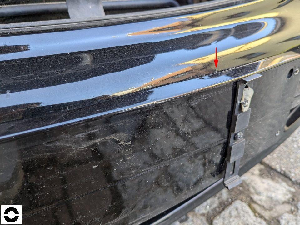 Frontstoßstange schwarz, Kratzer und Lackabrieb mit rotem Pfeil markiert, Kennzeichenhalter leer