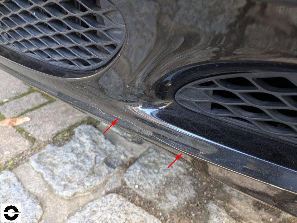 Frontstoßstange unten, Kratzer und Lackschäden an Chromleiste, rote Pfeile markieren Beschädigung