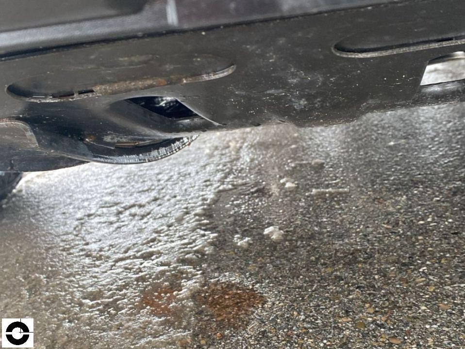 Unterbodenansicht mit Flüssigkeitsaustritt auf nassem Asphalt, möglicher Öl- oder Kühlmittelverlust