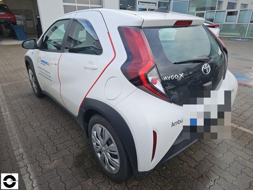 Heckansicht schräg rechts, weißer Toyota Aygo X mit Firmenbeschriftung, Kennzeichen pixeliert