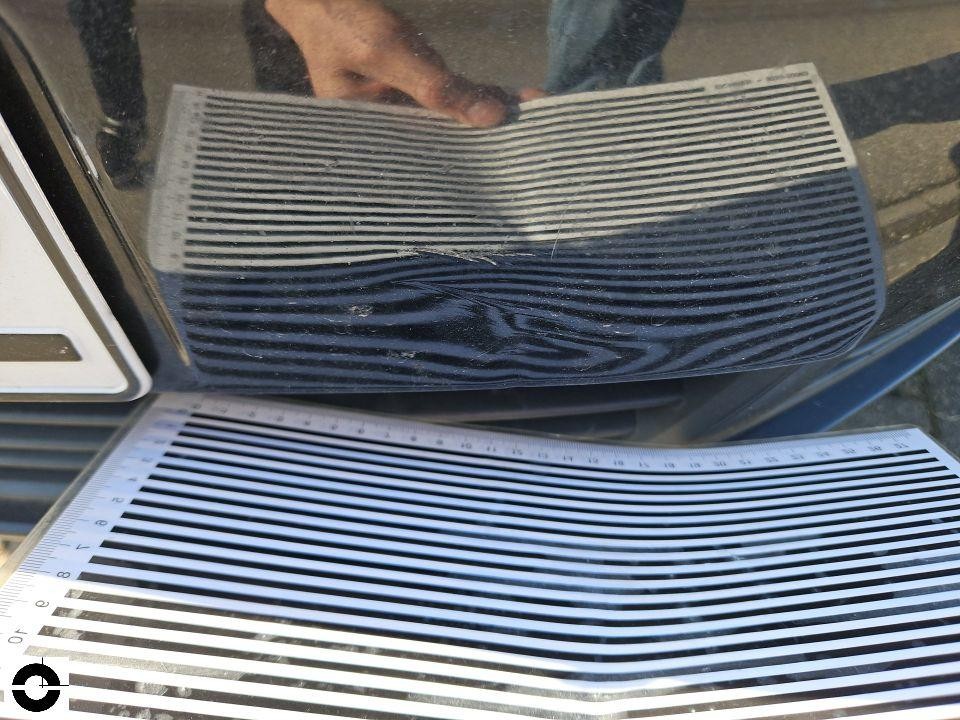 Dellenprüfung mit Streifenreflektor auf dunkler Motorhaube, Delle sichtbar