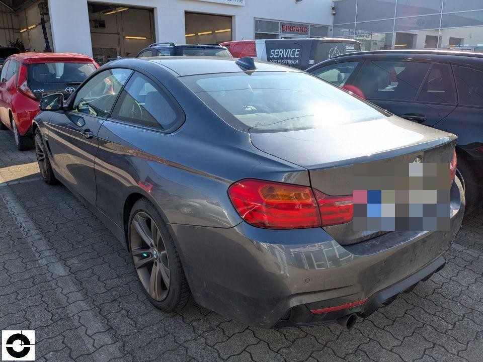 Heckansicht schräg von links, dunkles Coupé auf Parkplatz vor Autohaus