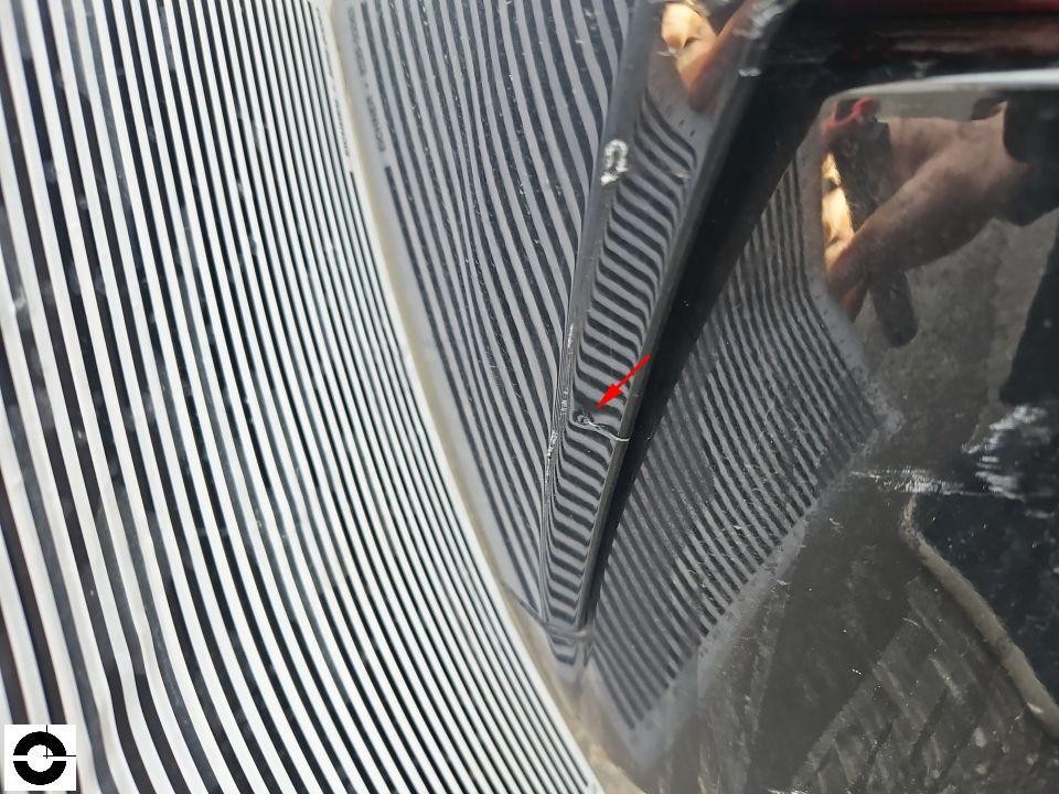 Nahaufnahme Frontgrill mit Lamellen und Scheinwerfer, roter Pfeil markiert Beschädigung