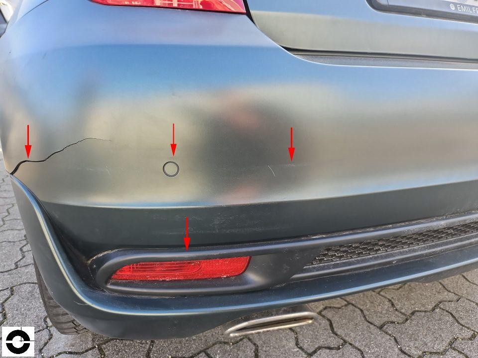Heckschürze mit Riss links, rote Pfeile markieren Kratzer und Beschädigungen
