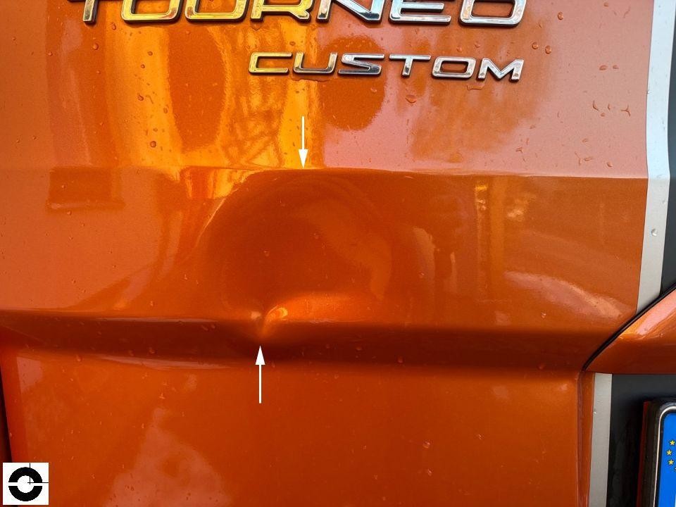 Heckansicht, Delle in Heckklappe unterhalb Tourneo Custom Schriftzug, mit Pfeilen markiert