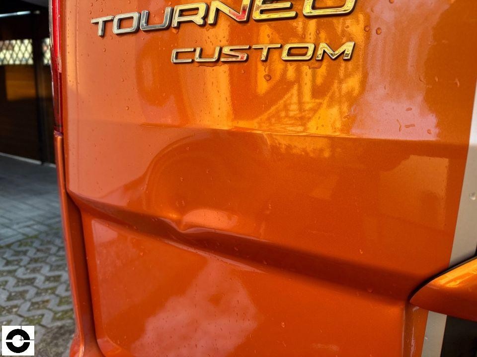 Heckansicht, orangefarbene Heckklappe mit Tourneo Custom Schriftzug, Regentropfen sichtbar