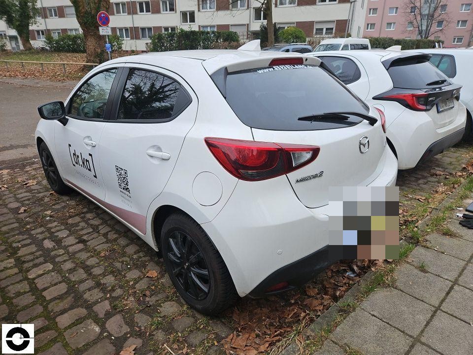 Heckansicht schräg links, weißer Mazda 2 mit Firmenbeschriftung, keine sichtbaren Schäden