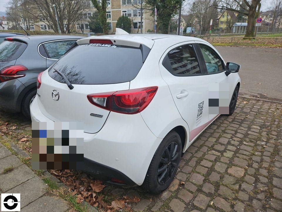 Heckansicht schräg rechts, weißer Kompaktwagen auf Kopfsteinpflaster, keine sichtbaren Schäden