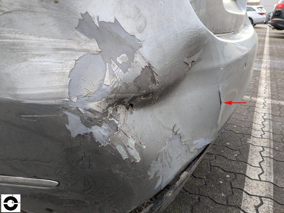 Hintere Stoßstange links mit starken Kratzern und Lackabplatzungen, roter Pfeil markiert Riss