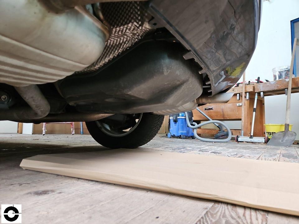 Unterboden-Ansicht von hinten, Auspuffanlage und Hinterrad sichtbar, Werkstattumgebung