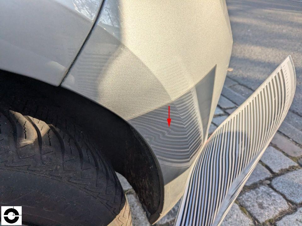 Kotflügel vorne links mit rotem Pfeil auf Delle/Verformung, Streifenlichtanalyse sichtbar