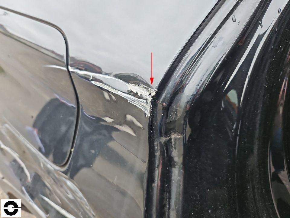 Detailaufnahme Lackschaden an hinterer Kotflügelkante links, abgeplatzte Farbe mit rotem Markierungspfeil