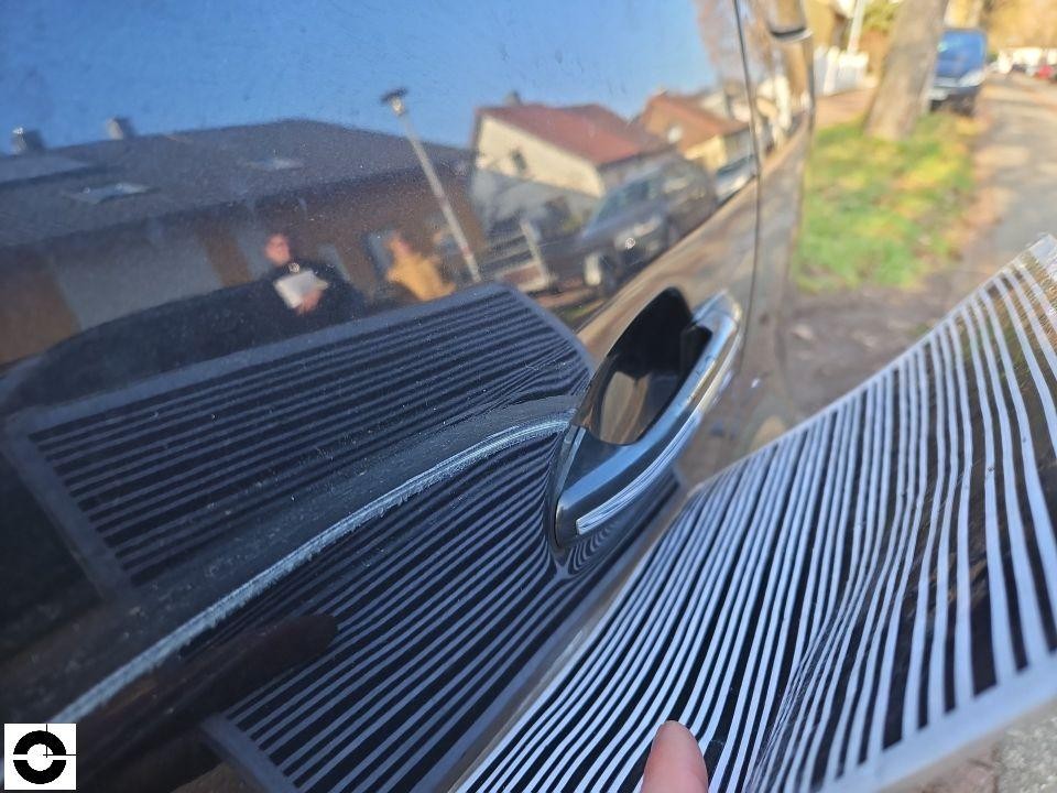 Heckscheibe mit Heizungslamellen und Türgriff, Spiegelung zeigt Umgebung