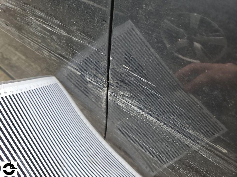 Detailaufnahme von Kratzern und Schleifspuren auf schwarzer Lackoberfläche mit Lineal zur Dokumentation