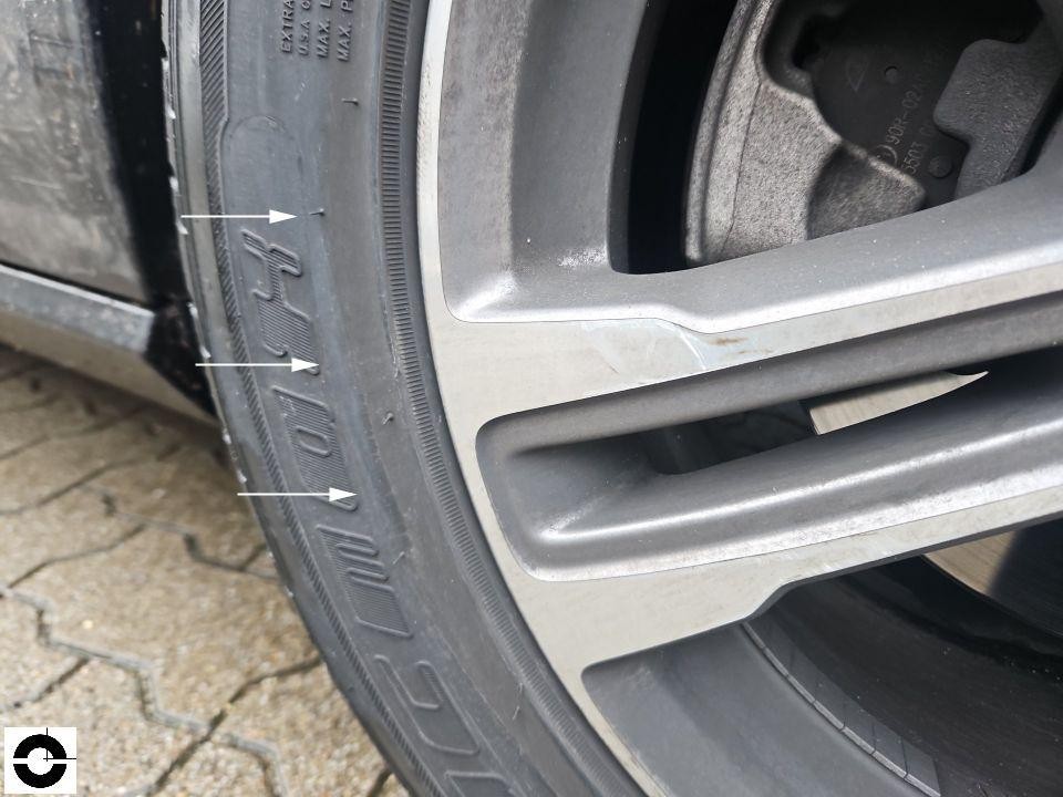 Nahaufnahme Alufelge mit Bordsteinschaden, Pfeile markieren Kratzer an Felgenkante