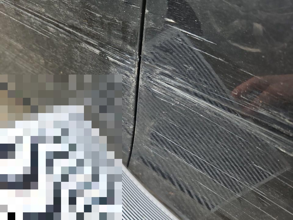 Nahaufnahme Kratzer und Schleifspuren auf schwarzer Karosserie, Stoßfängerbereich