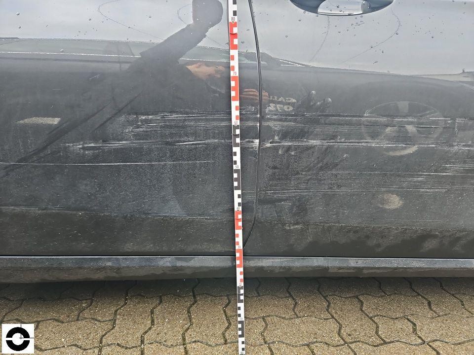 Seitenansicht linke Fahrzeugseite mit Schleifspuren und Kratzern an Vorder- und Hintertür, Messlatte zur Schadendokumentation