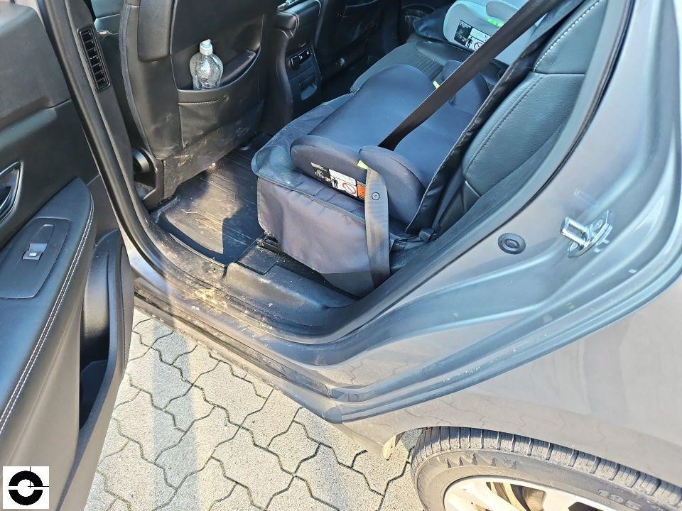 Blick auf Rücksitzbereich mit Kindersitzerhöhung, verschmutzter Fußraum, geöffnete hintere Tür