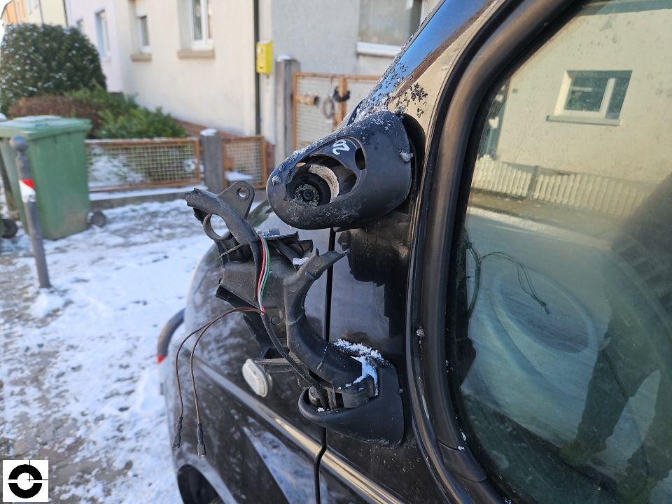 Zerstörter linker Außenspiegel mit freiliegenden Kabeln und Halterung, Nahaufnahme
