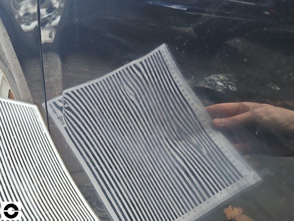 Dellenprüfung mit Streifenspiegel an dunkler Karosserie, Hand hält Prüffolie