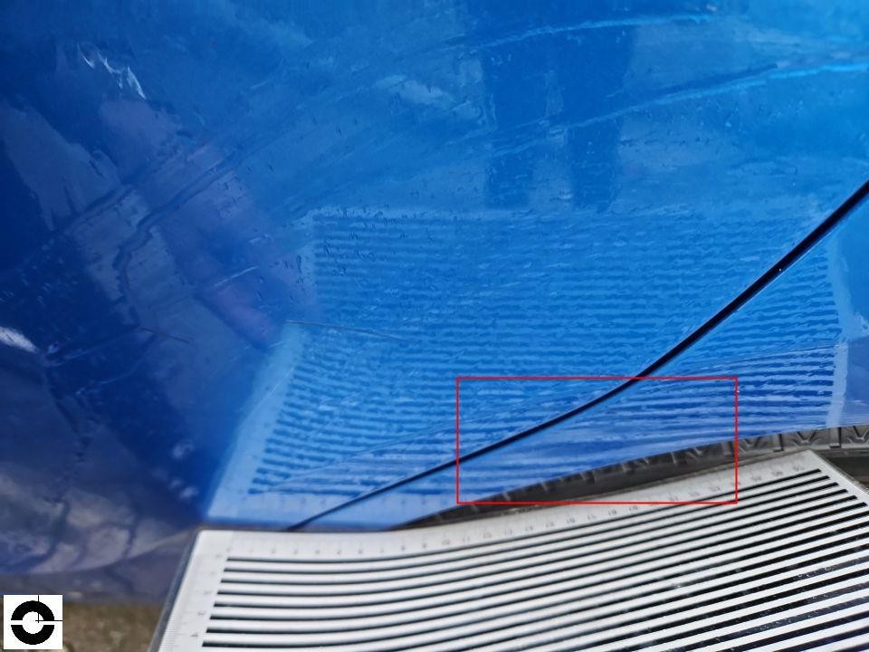 Detailaufnahme der Motorhaube mit Kratzern und Lackschäden, blau lackiert, mit Messlatte
