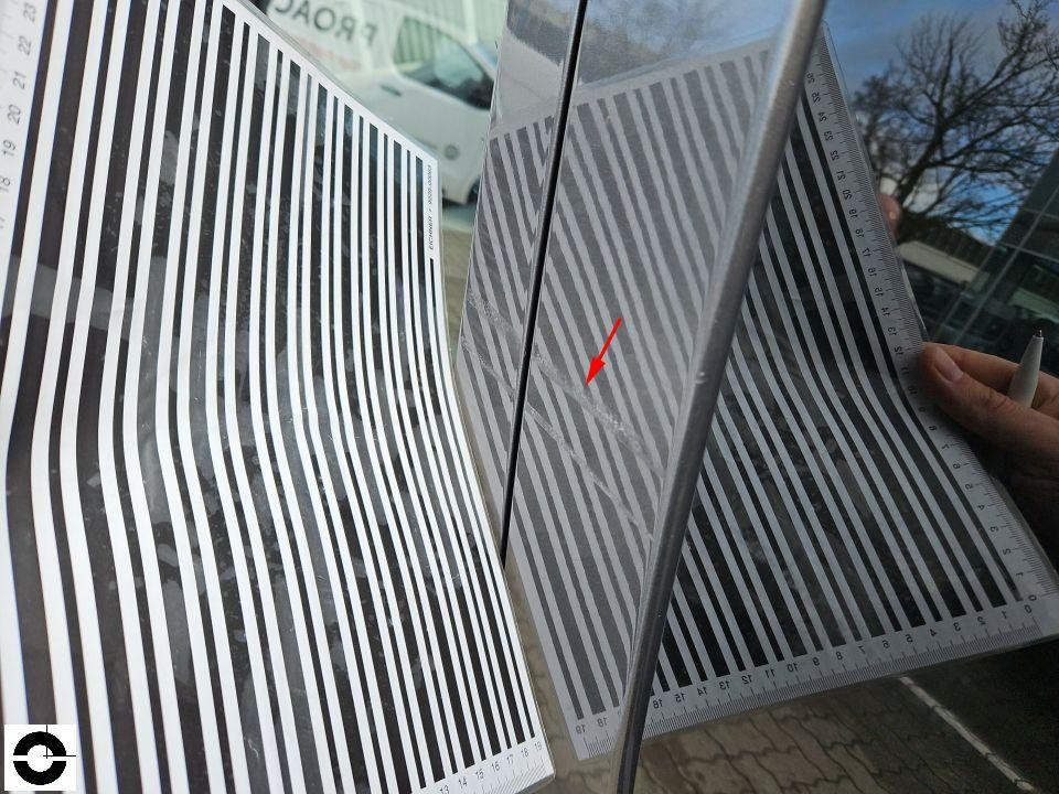 Dellenprüfung mit Streifentafel an Fahrzeugseite, roter Pfeil markiert Schadenstelle
