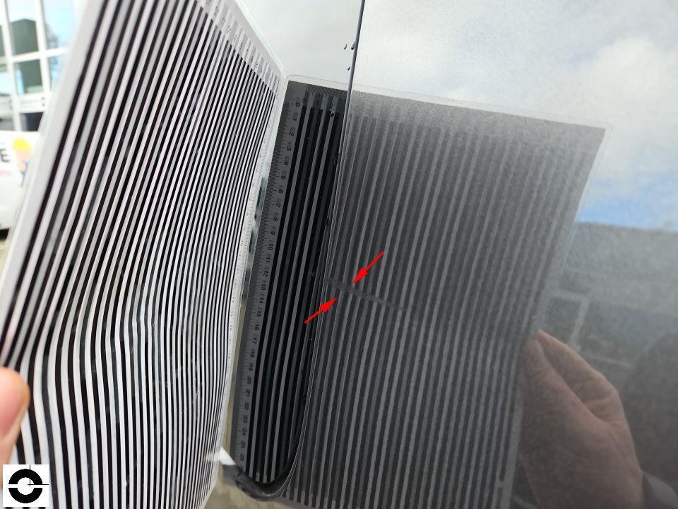 Windschutzscheibe mit Streifenfolie zur Schadensdokumentation, roter Pfeil markiert Steinschlag