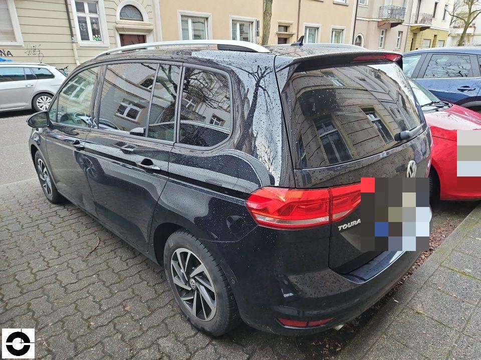 Heckansicht schräg links, schwarzer VW Touran, nasse Oberfläche, keine sichtbaren Schäden