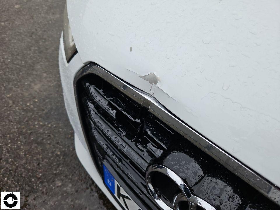 Frontpartie mit Lackabplatzung an Motorhaubenkante über Kühlergrill, Regentropfen sichtbar