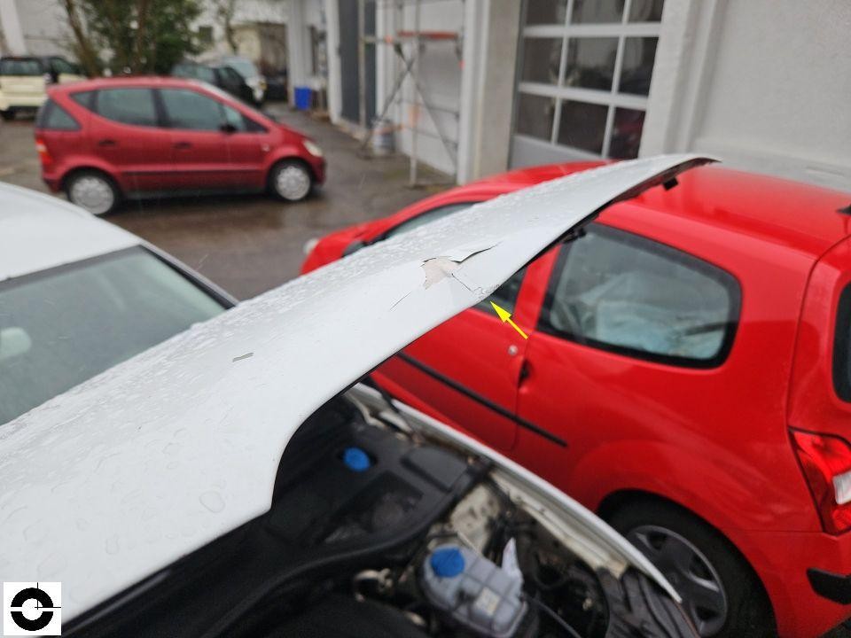 Geöffnete Motorhaube mit Lackschaden und Aufwerfung, gelber Pfeil markiert Beschädigung
