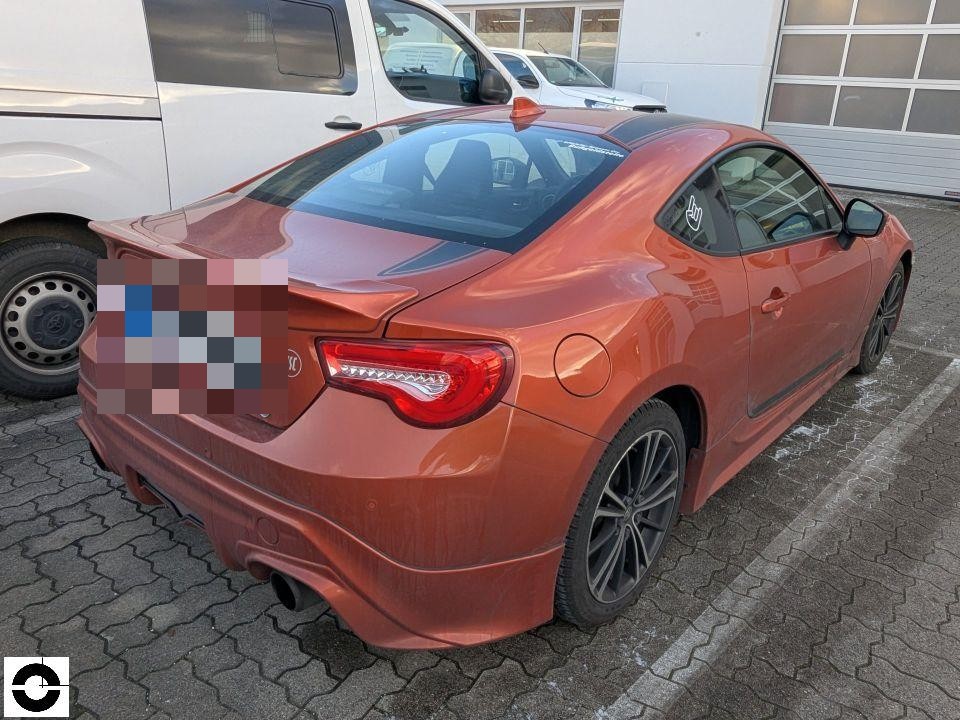 Heckansicht schräg links, orangefarbenes Sportcoupé, keine sichtbaren Schäden