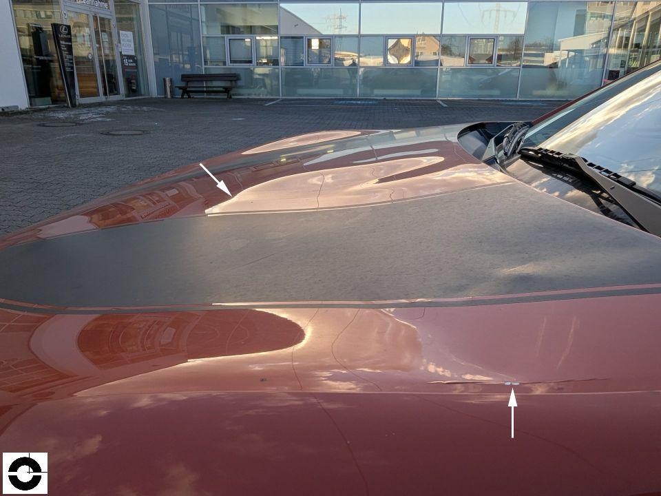 Motorhaube von vorne, zwei weiße Pfeile markieren Kratzer/Beschädigungen auf der Lackoberfläche