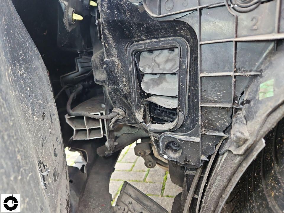 Detailaufnahme Motorraum vorne links, stark verschmutzter Scheinwerferbereich mit freiliegenden Kabeln und beschädigten Kunststoffteilen