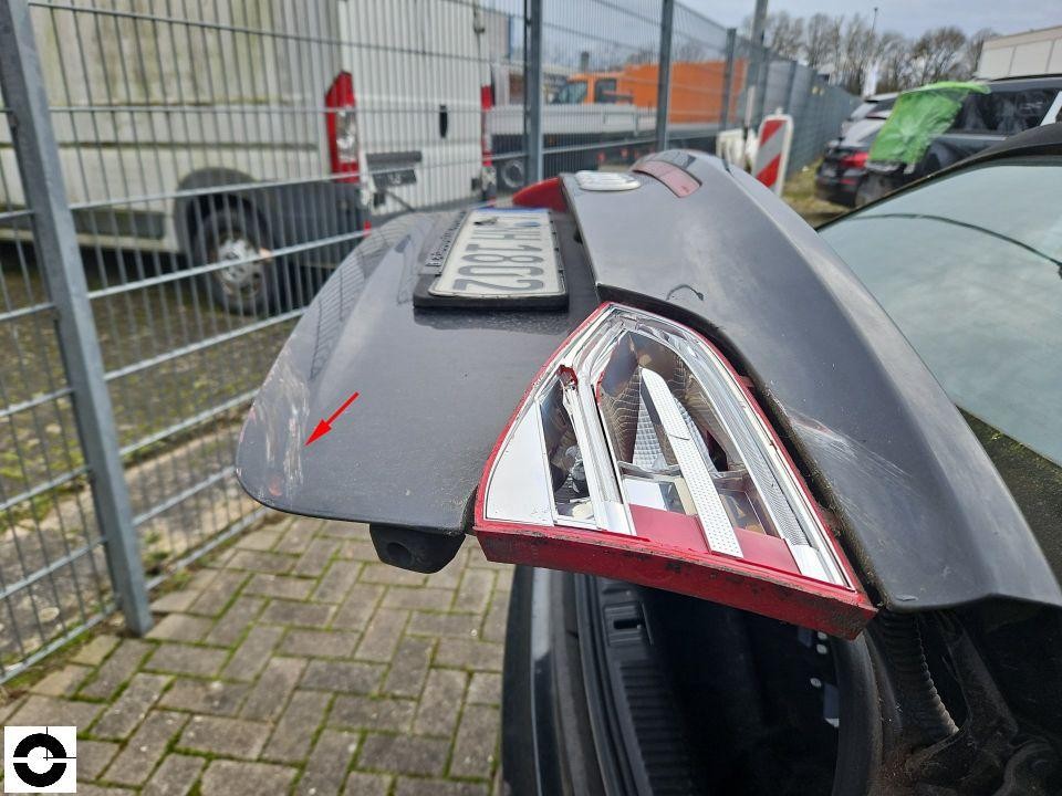 Geöffnete Heckklappe mit beschädigter rechter Rückleuchte, roter Pfeil markiert Delle