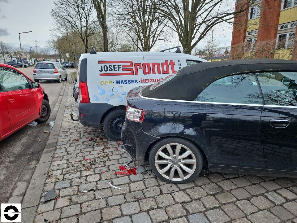 Unfallszene mit mehreren Fahrzeugen, Heckschaden am schwarzen Fahrzeug, Trümmerteile auf Pflaster