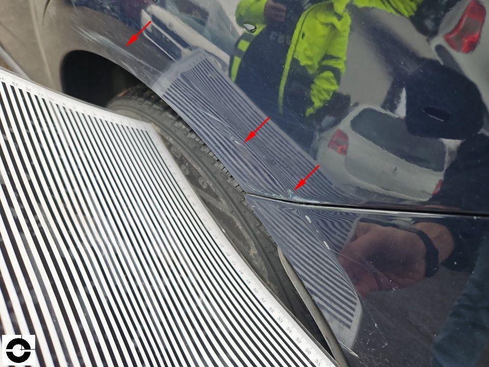 Detailaufnahme Motorhaube mit Dellen, rote Pfeile markieren Schadenstellen, Streifenlicht-Reflexion