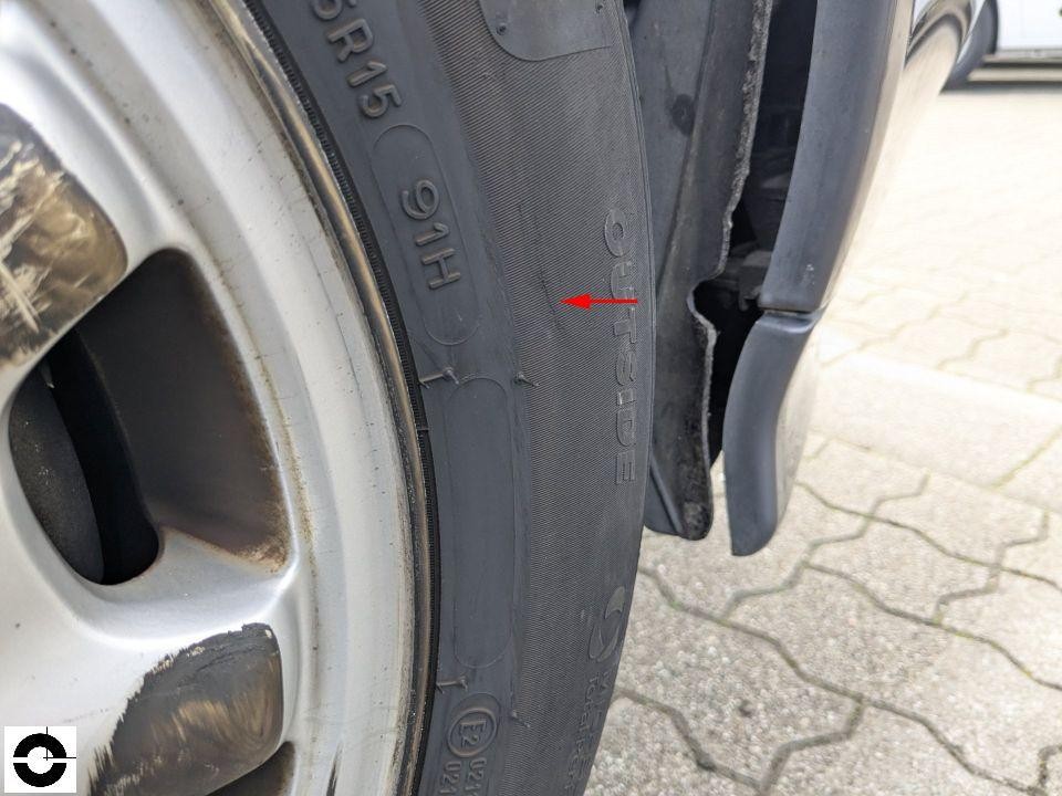 Detailaufnahme Reifen mit rotem Pfeil auf Beschädigung/Schnitt in der Seitenwand