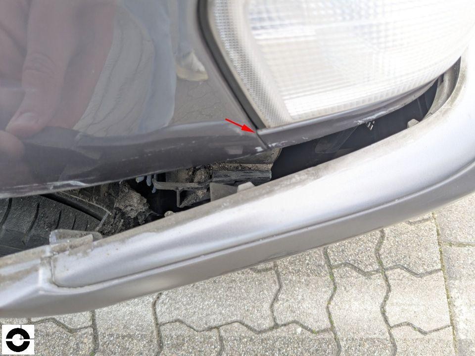 Frontstoßstange links, Spalt zwischen Stoßfänger und Scheinwerfer, roter Pfeil markiert Beschädigung