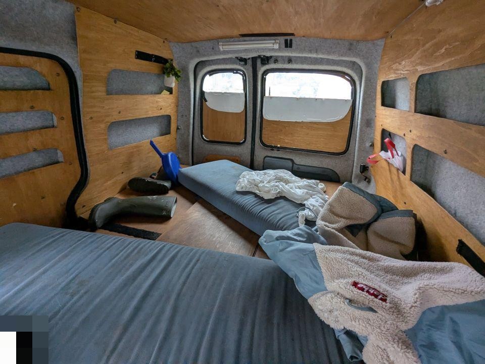 Innenraum eines ausgebauten Transporters mit Schlafbereich, Holzverkleidung und Matratzen