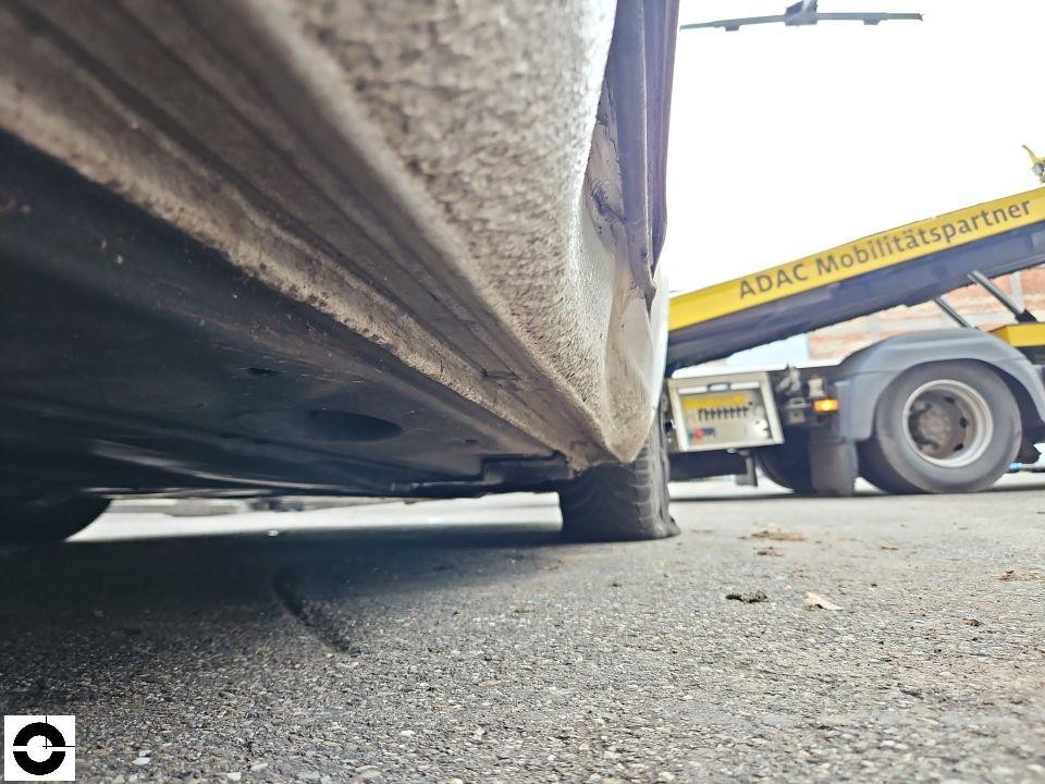 Unterbodenperspektive, Schwellerbereich mit Schmutz und Korrosion, ADAC-Abschleppfahrzeug im Hintergrund